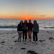 Four people smiling with the ocean and sunset in the background; photo from a distance