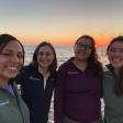 Four people smiling with the ocean and sunset in the background; selfie angle