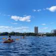 Several orange kayaks on the water, the MIT dome in the distance